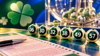 Bolas de loteria com as dezenas 06, 30, 32, 38, 49 e 57, ao lado de um volante de apostas e um globo de sorteio ao fundo.